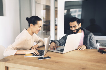 Smiling business people looking at laptop computers while sitting in office - CAVF25616