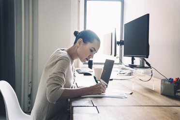 Side view of businesswoman writing while sitting at desk in office - CAVF25622