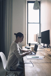 Seitenansicht einer Geschäftsfrau, die einen Laptop benutzt, während sie am Schreibtisch im Büro sitzt - CAVF25623