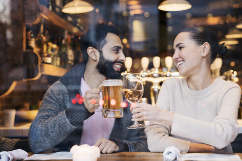 Glückliches Paar stößt auf Getränke an, gesehen durch ein Restaurantfenster - CAVF25644