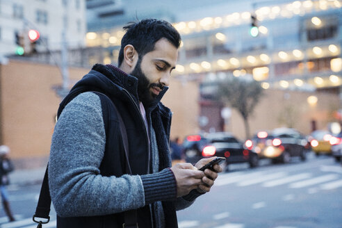 Mann, der ein Mobiltelefon benutzt, während er in der Abenddämmerung auf einer Straße in der Stadt steht - CAVF25647