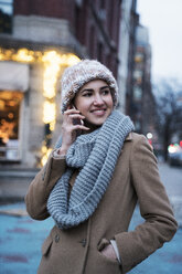 Lächelnde Frau, die in der Dämmerung in der Stadt mit einem Mobiltelefon spricht - CAVF25649