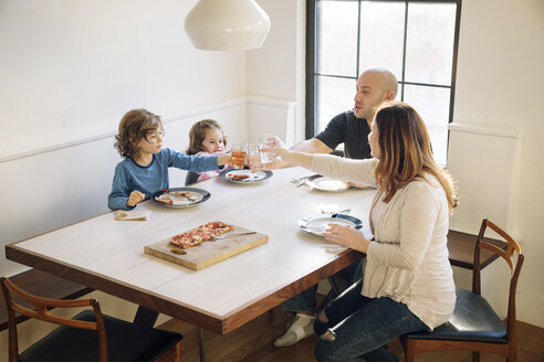 Familie erhebt feierlich einen Toast, während sie zu Hause am Esstisch sitzt - CAVF25661