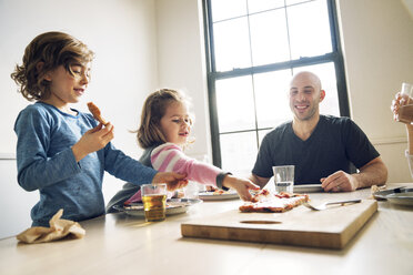 Girl picking pizza slice while sitting with family at dining table in home - CAVF25662