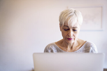 Ältere Frau, die zu Hause einen Laptop an der Wand benutzt - CAVF25670