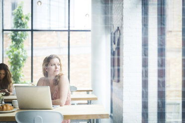 Thoughtful woman at cafe with friend in background seen through window - CAVF25869