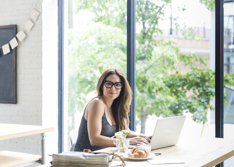 Porträt einer selbstbewussten Frau, die einen Laptop benutzt und in einem Café am Fenster sitzt - CAVF25872