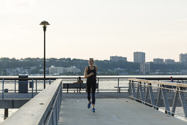 Woman jogging while exercising on bridge against clear sky in city - CAVF25884