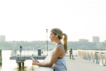 Side view of woman looking away while listening music on bridge against clear sky - CAVF25900