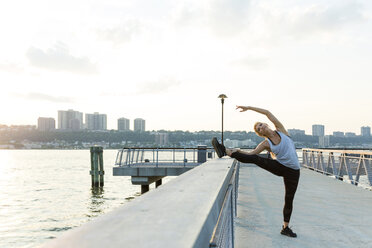 Full length of woman stretching leg on railing at bridge against sky in city - CAVF25901