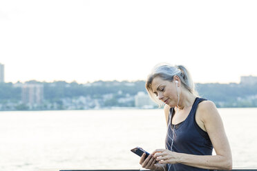 Frau mit Smartphone beim Hören von Musik auf einer Brücke gegen den klaren Himmel - CAVF25905