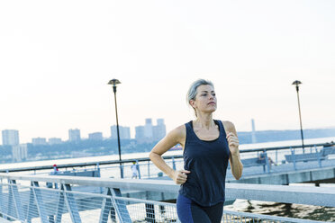 Frau beim Joggen auf einer Brücke gegen den klaren Himmel - CAVF25908