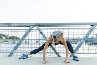 Full length of confident woman exercising on bridge against clear sky - CAVF25914