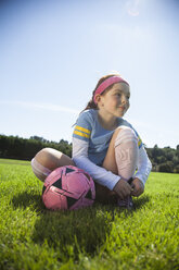 Mädchen bindet Schnürsenkel, während sie mit einem Ball auf einer Wiese sitzt - CAVF25922