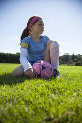Girl with soccer ball looking away while sitting on grassy field - CAVF25923