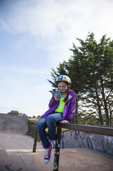 Mädchen, das ein Mobiltelefon benutzt, während es auf einem Geländer gegen den Himmel sitzt - CAVF25926