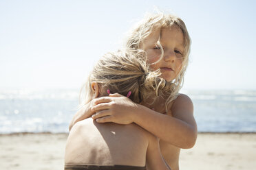 Schwestern umarmen sich am Strand an einem sonnigen Tag - CAVF25931