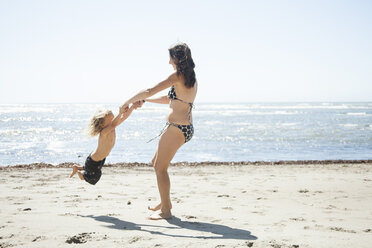 Happy mother playing with daughter at beach against clear sky - CAVF25932