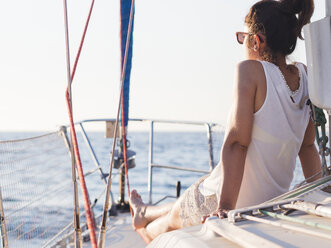 Rückansicht einer mittleren erwachsenen Frau, die auf das Meer blickt, während sie in einem Segelboot gegen den klaren Himmel sitzt - CAVF25940