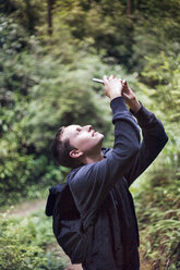 Seitenansicht eines Mannes, der mit seinem Smartphone im Wald fotografiert - CAVF25957