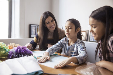 Smiling mother and daughter looking at girl making paper flowers - CAVF26043