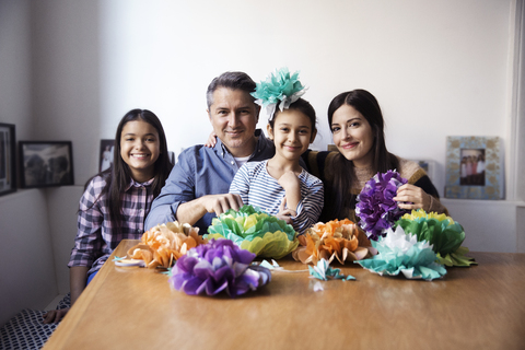 Portrait of family with paper flowers sitting at table against wall stock photo