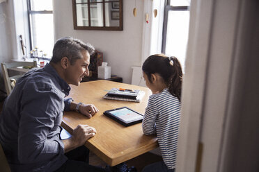 Father looking at girl using tablet computer seen through doorway - CAVF26053