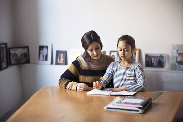 Mother assisting daughter for studying while sitting at table - CAVF26054