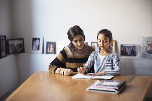 Mutter, die ihrer Tochter beim Lernen hilft, während sie am Tisch sitzt - CAVF26054