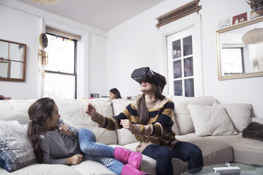 Tochter schaut auf ihre Mutter, die auf dem Sofa sitzend einen Virtual-Reality-Simulator genießt - CAVF26063