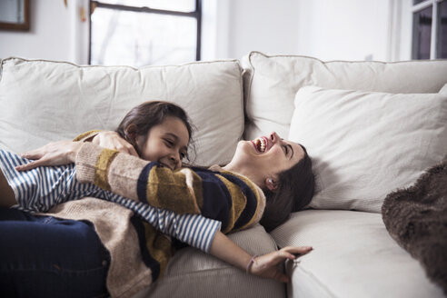 Cheerful mother and daughter enjoying on sofa at home - CAVF26064