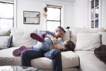 Fröhlicher Vater spielt mit Tochter auf Sofa zu Hause - CAVF26066