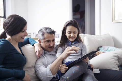 Familie benutzt Tablet-Computer, während sie zu Hause auf dem Sofa sitzt, lizenzfreies Stockfoto