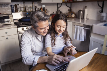 Hoher Blickwinkel von Vater und Tochter, die einen Laptop in der Küche zu Hause benutzen - CAVF26076