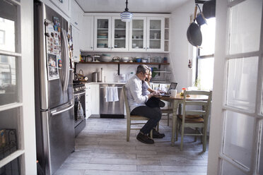 Side view of father and daughter using laptop computer in kitchen at home - CAVF26077