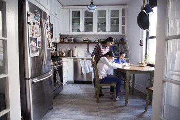 Frau, die ihren Töchtern beim Lernen am Küchentisch hilft - CAVF26091
