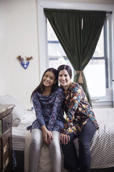 Porträt von Mutter und Tochter, die zu Hause auf dem Bett sitzen - CAVF26098