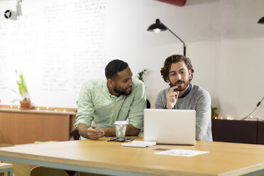 Businessman discussing with colleague while using laptop computer in office - CAVF26100