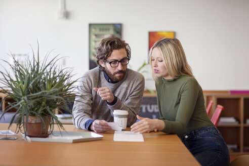 Kollegen diskutieren am Tisch sitzend im Büro - CAVF26112