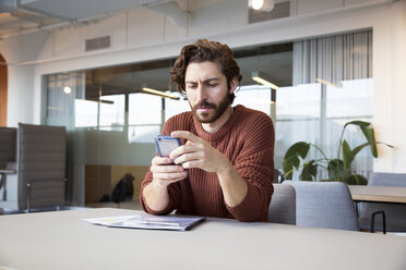 Confident businessman using mobile phone at table in office - CAVF26123