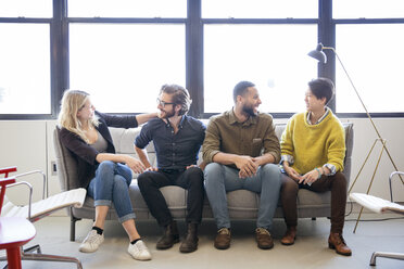 Happy business people talking while sitting on sofa in office - CAVF26132