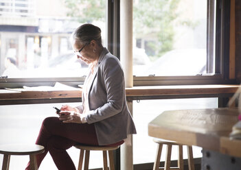 Reife Frau telefoniert, während sie am Tisch im Café sitzt - CAVF26153