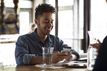 Smiling young man using phone at bar counter in cafe - CAVF26161