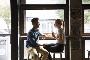 Lächelndes Paar, das sich am Fenster eines Cafés unterhält - CAVF26163