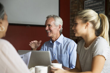 Smiling businessman talking to colleagues during meeting at cafe - CAVF26166