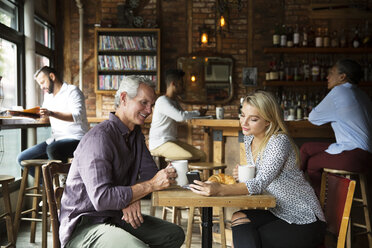 Woman showing phone to man while customers relaxing at cafe - CAVF26177