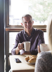 Reifer Mann im Gespräch mit einer Frau bei einem Kaffee am Fenster eines Cafés - CAVF26178