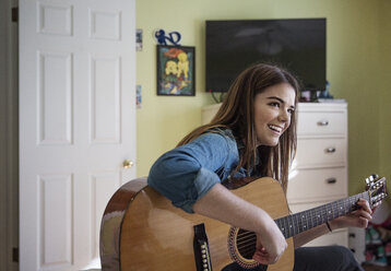 Glückliche Frau spielt Gitarre, während sie zu Hause sitzt - CAVF26193