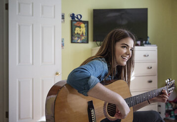 Happy woman playing guitar while sitting at home - CAVF26193