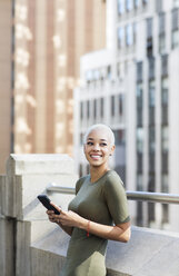 Lächelnde Geschäftsfrau, die auf dem Balkon eines Büros ein Mobiltelefon benutzt - CAVF26222